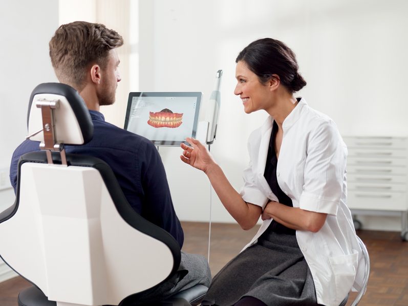 Zahnärztin zeigt Patient auf Tablet Informationen zur Behandlung.